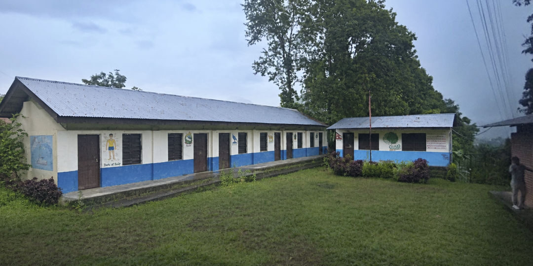 Einstöckige Schulgebäude mit blauen Türen umgeben einen grünen Innenhof.