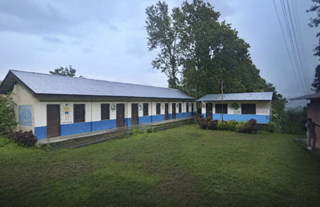 Einstöckige Schulgebäude mit blauen Türen umgeben einen grünen Innenhof.