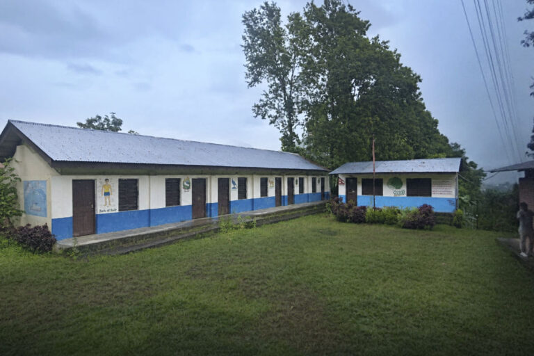 Einstöckige Schulgebäude mit blauen Türen umgeben einen grünen Innenhof.